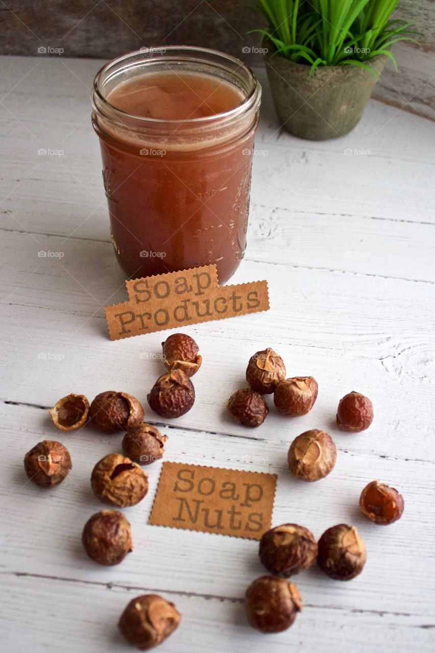 Closeup of soap nuts or soap berries with label and liquid soap for DIY soap products on white wooden surface in natural light