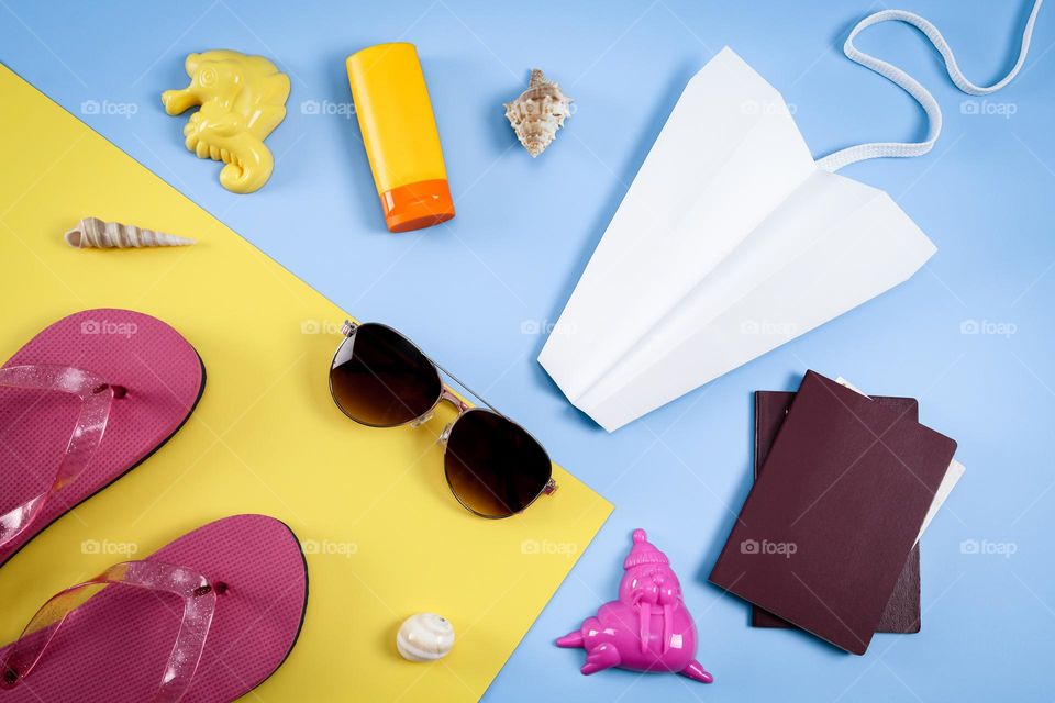 Sunglasses,passport,pink flip flops, paper plane, tube of sun cream, sand toys and seashells lie on the wall on a yellow background, flat lay close up.