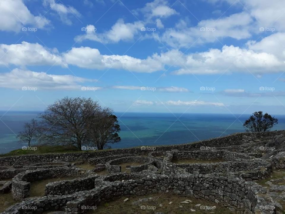 Un castro (archaeological ruins from an iron age settlement) on a hillside overlooking the beautiful blue and green sea.  Clouds and a tree are present.  
One of the most peaceful places I have ever been to.❤