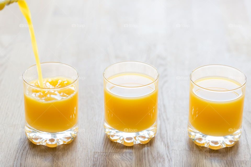 Three glasses filled with cold orange juice on a wooden table indoors 