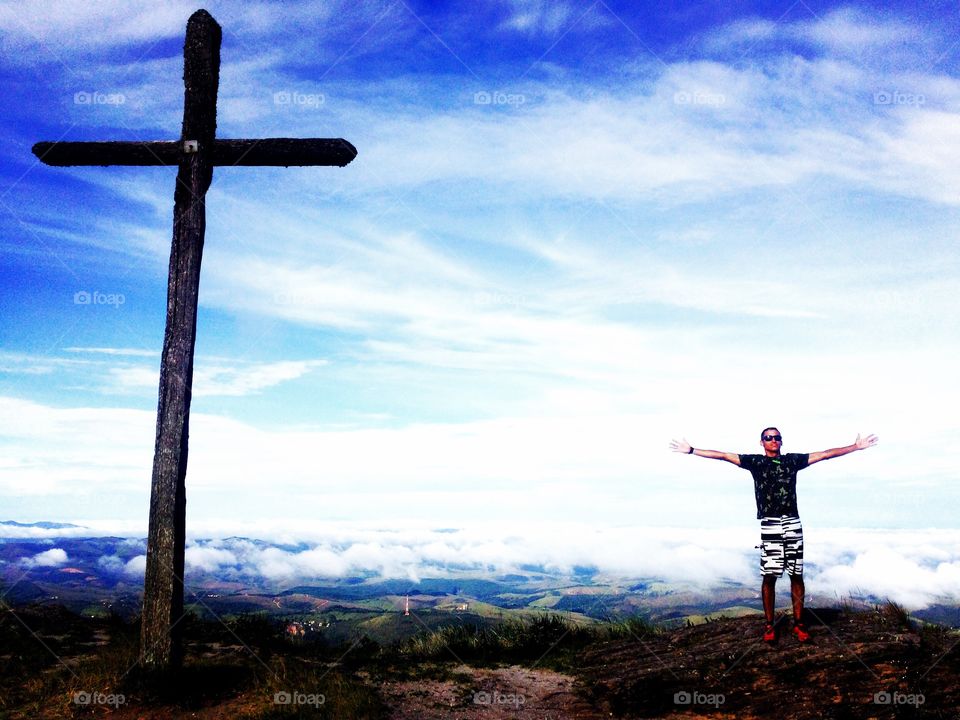 Young man standing on mountain in front of wooden cross