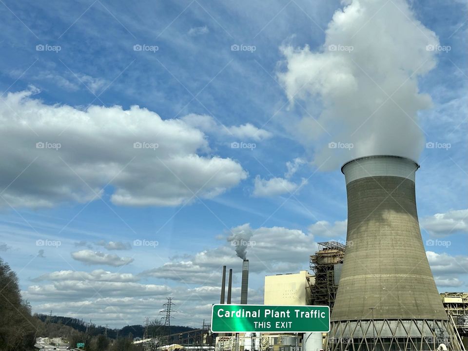 Beautiful blue sky with white fluffy clouds and power plant with white smoke coming from it 