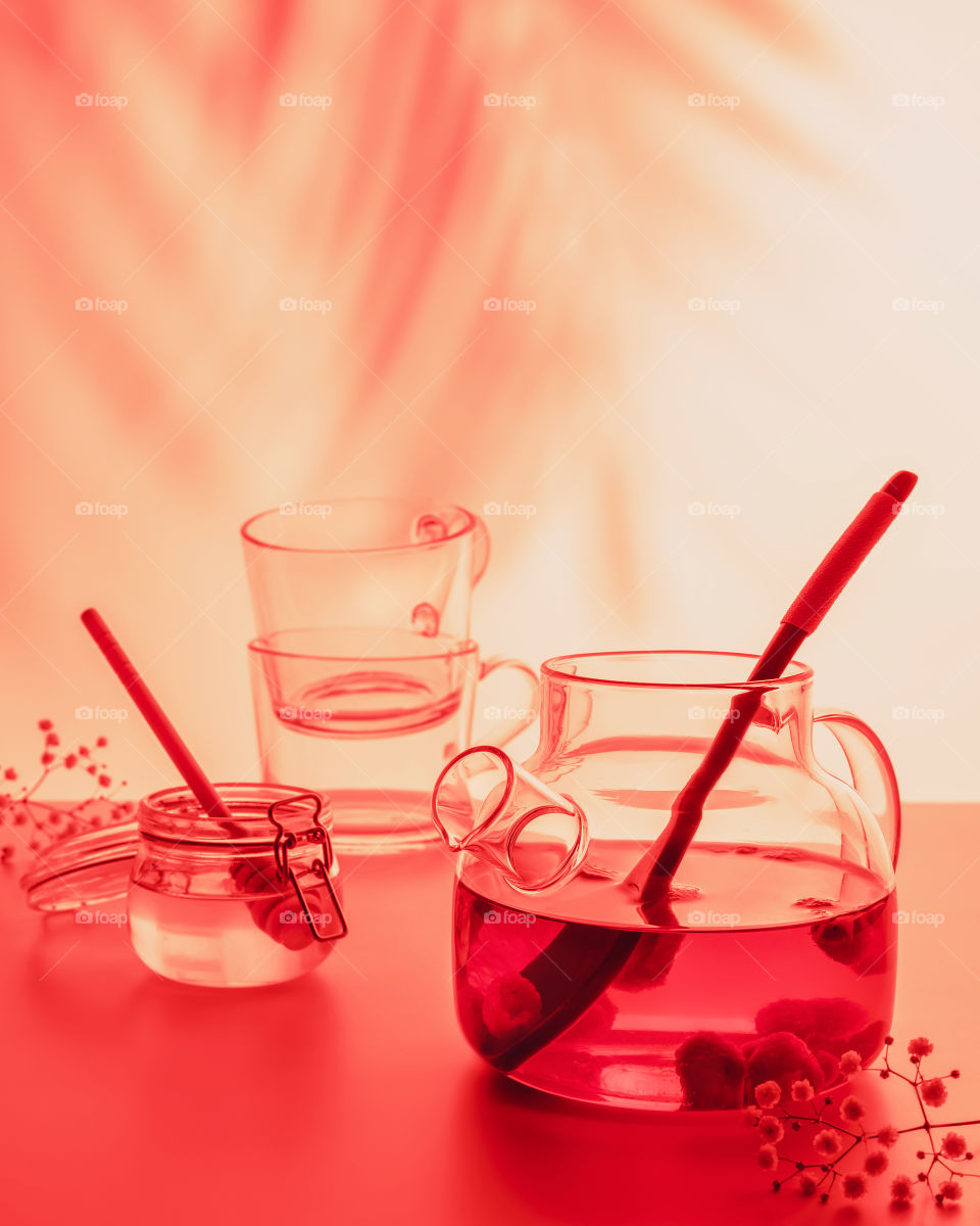 Blurred fruit tea composition with glass teapot, jar with honey and two glass cups on light sunset background with palm shadows. Summer relax tea party. Healthy no alcohol natural drink