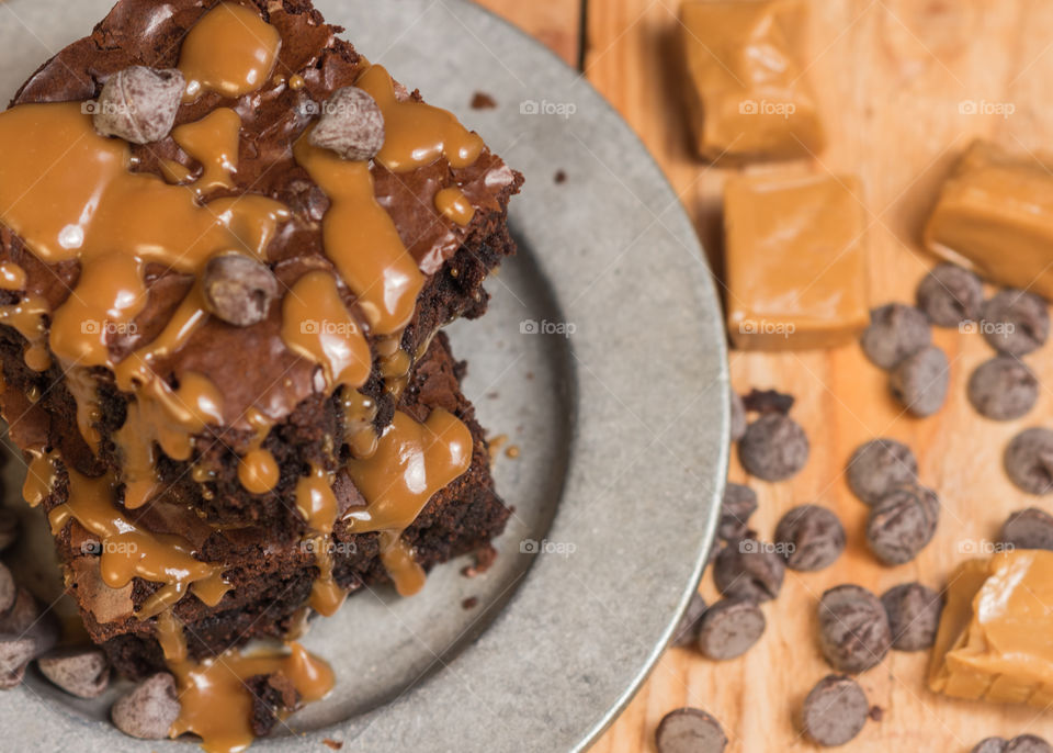 brownies baked with caramel and chocolate served on a pewter plate and placed on a wood table with caramel and chocolate chips scattered