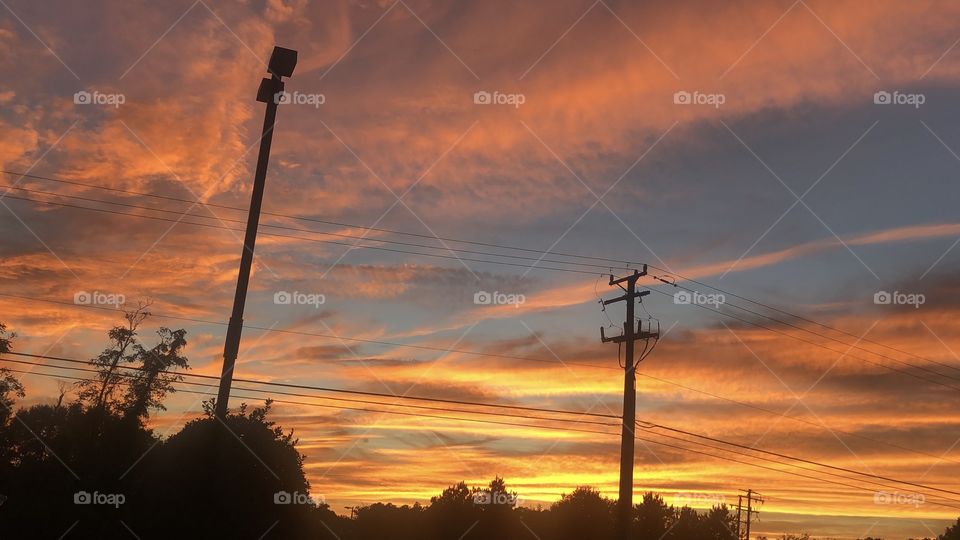 gorgeous sunset firey sky silhouette power lines and trees in the distance blue and yellow and pink sky