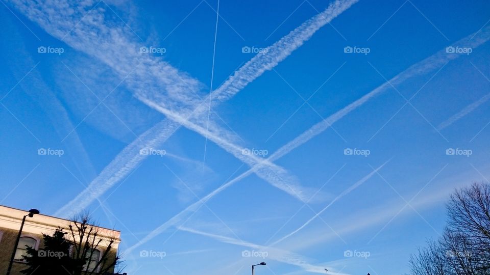 Aircraft smoke trails creating three crosses in the blue sky above Tally Ho Corner, North Finchley, London
