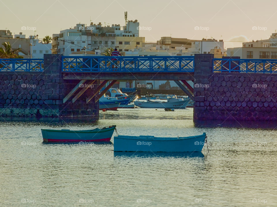 Paisaje clásico de botes en el agua con un puente de fondo con luz del atardecer, tomada en la isla de Lanzarote en el charco de san gines