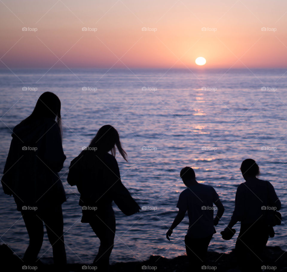 silhouettes of four people walking towards the sunset at the beach