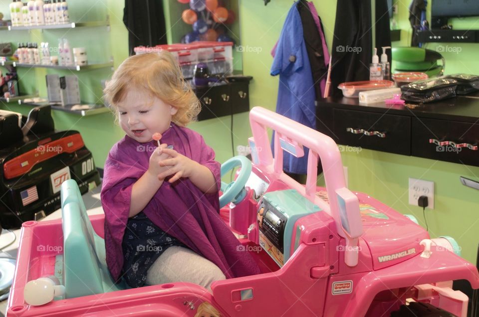 Girl sitting in kid's salon with lollipop candy in hand