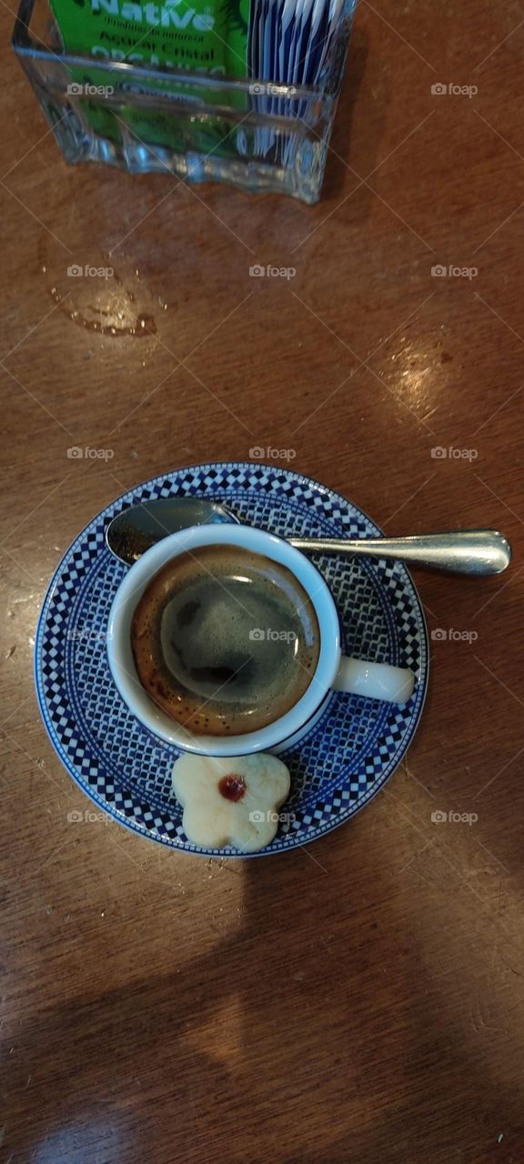 Coffee in the blue cup made from fresh beans by Brazilian traditional recipe. 
Spoon and cookie on the dish.