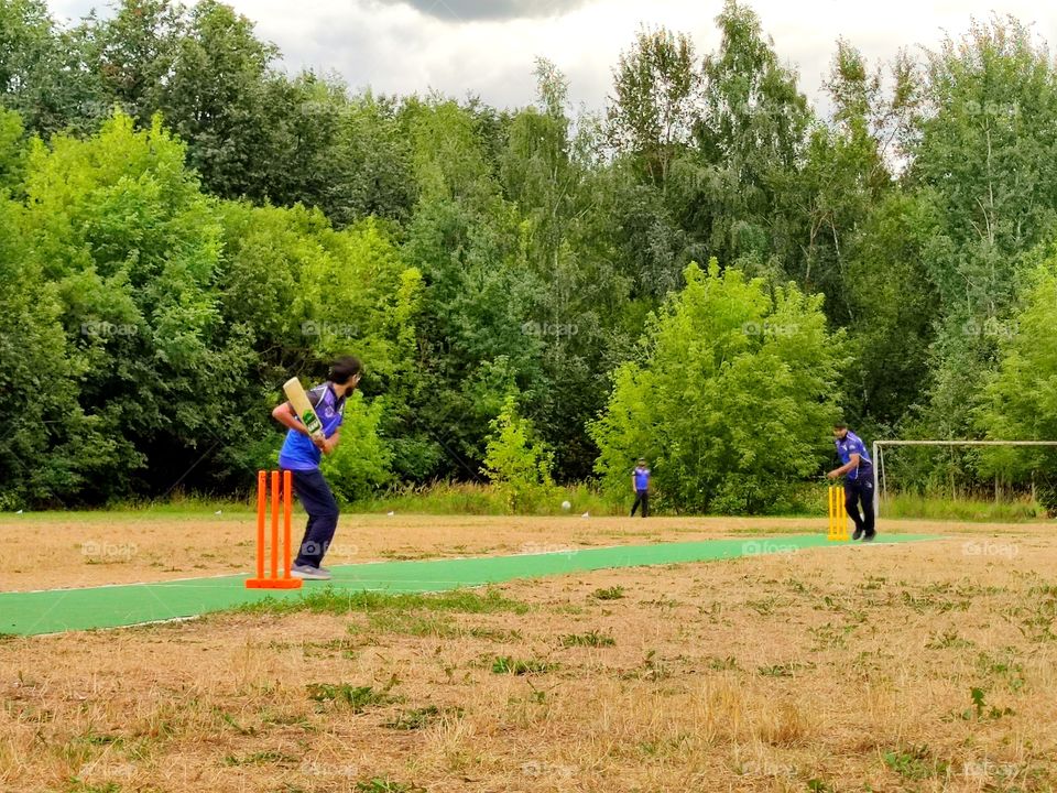 cricket training.  one player threw the ball, the second player in a standing position to hit the ball.  white ball flies in the middle of the field