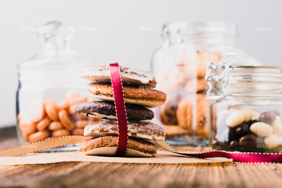 A few gingerbread cookies wrapped in red ribbon Happy Christmas on wooden table. Jars with sweets in the background