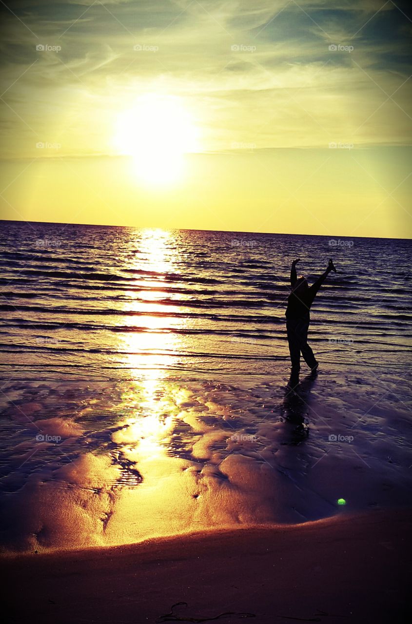 Rejoicing figure finds happiness walking on the beach at sunset.
