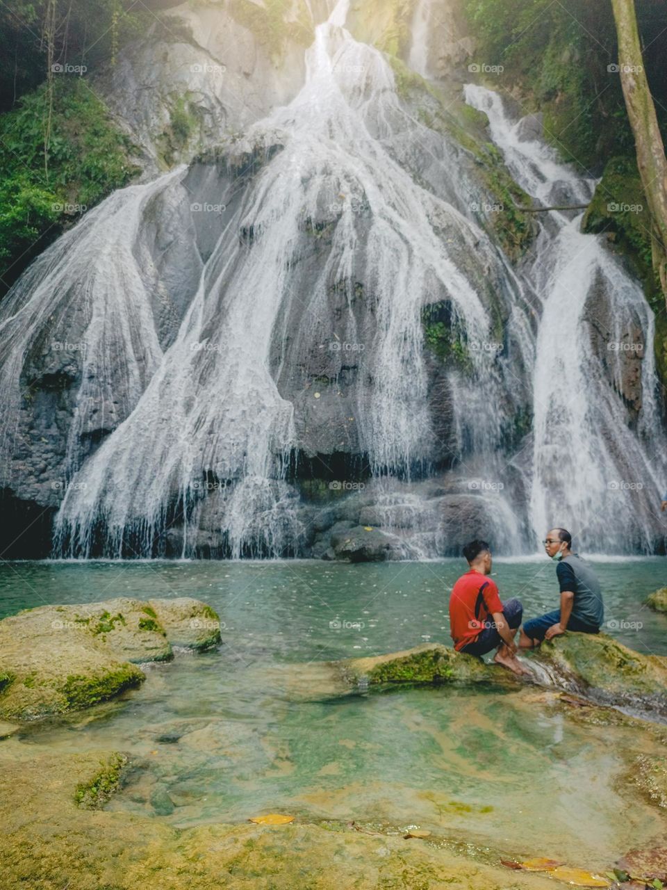 Couple men's sitting on rock in Taeno waterfall, Ambon Maluku, Indonesia, May 27, 2023