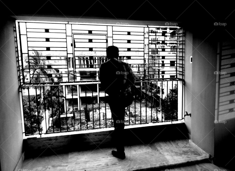 Man breathing fresh air standing on balcony of his apartment, black & white potrait back view captured.
