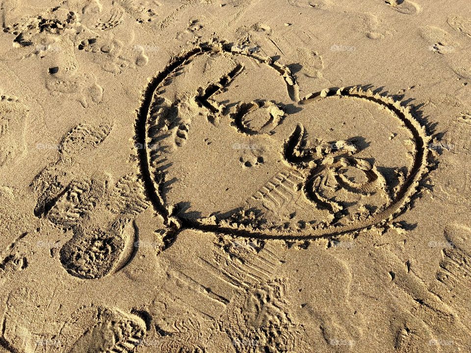 Love and heart finger drawing in the beach sand. Footprints. Brown overall color.