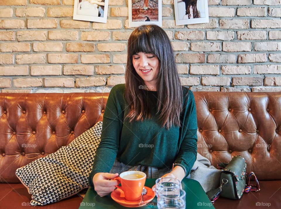 Young woman sitting in stylish cafe, drinking coffee from an orange cup