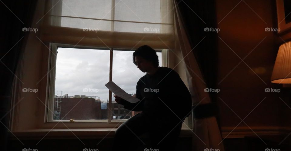 Side View Of Silhouette Man Reading Book While Sitting By Window At Home