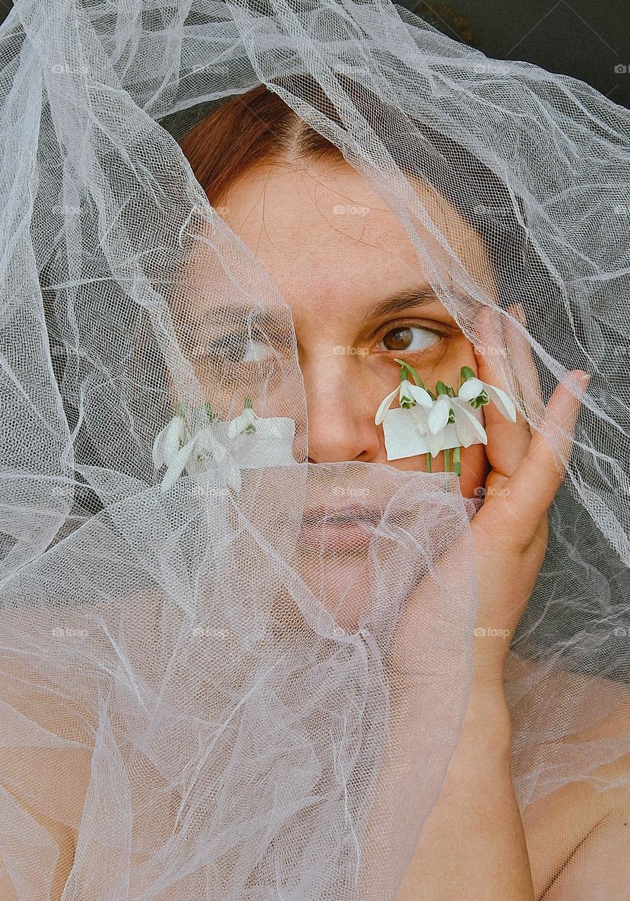 original portrait of a young girl without makeup with problematic skin with the first spring flowers on her face, namely white snowdrops