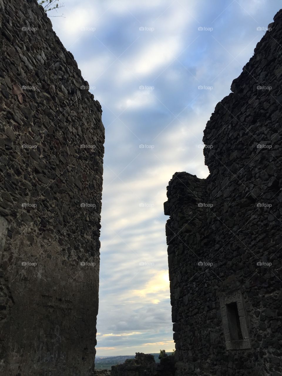 A passage between two rocky walls of ruins of Nevytsky Castle against the sky on sunset