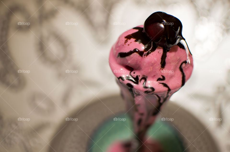 Beautiful pink ice cream melting with fresh cherry on top smothered in chocolate 