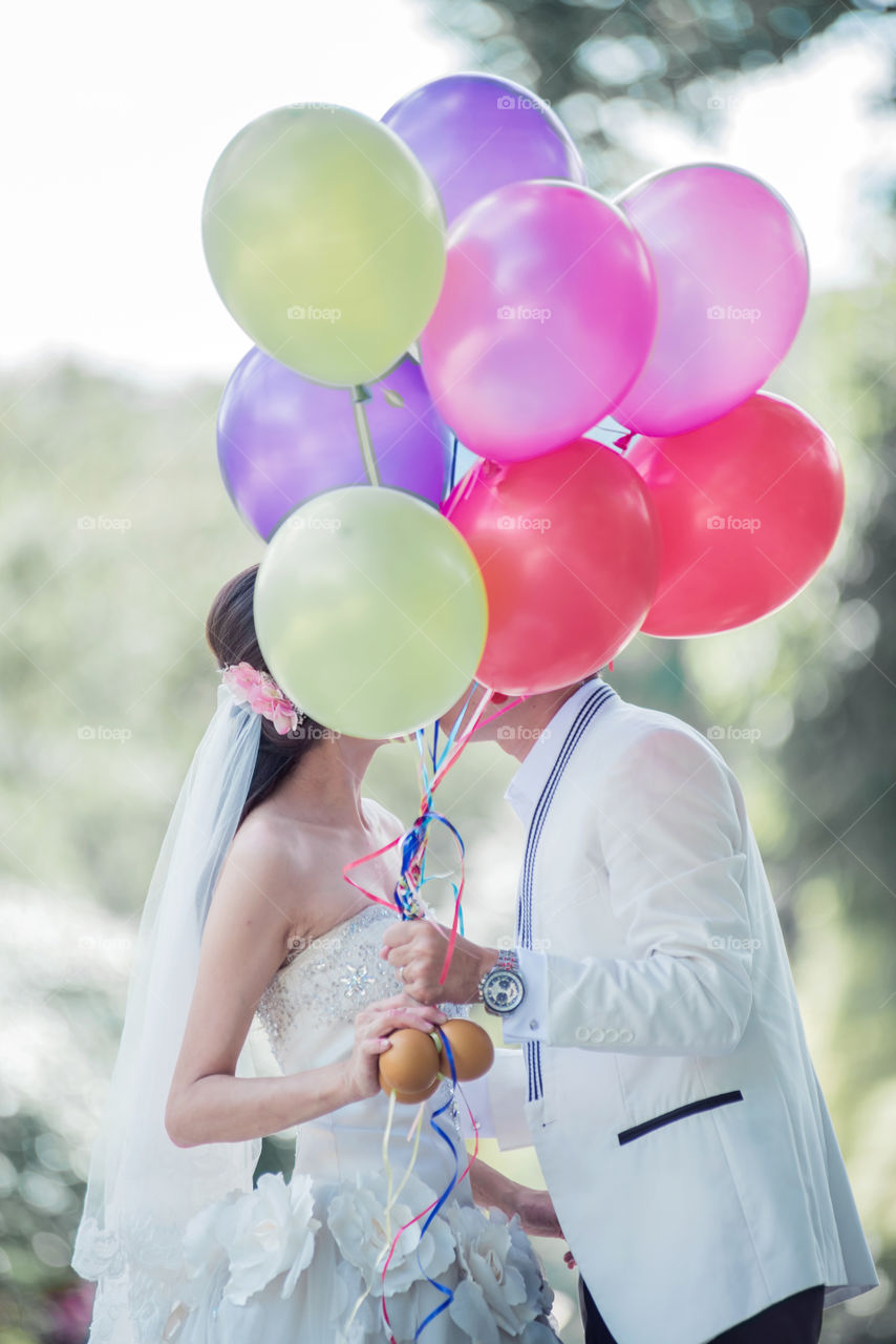 Couple kissing behind multi colored balloons