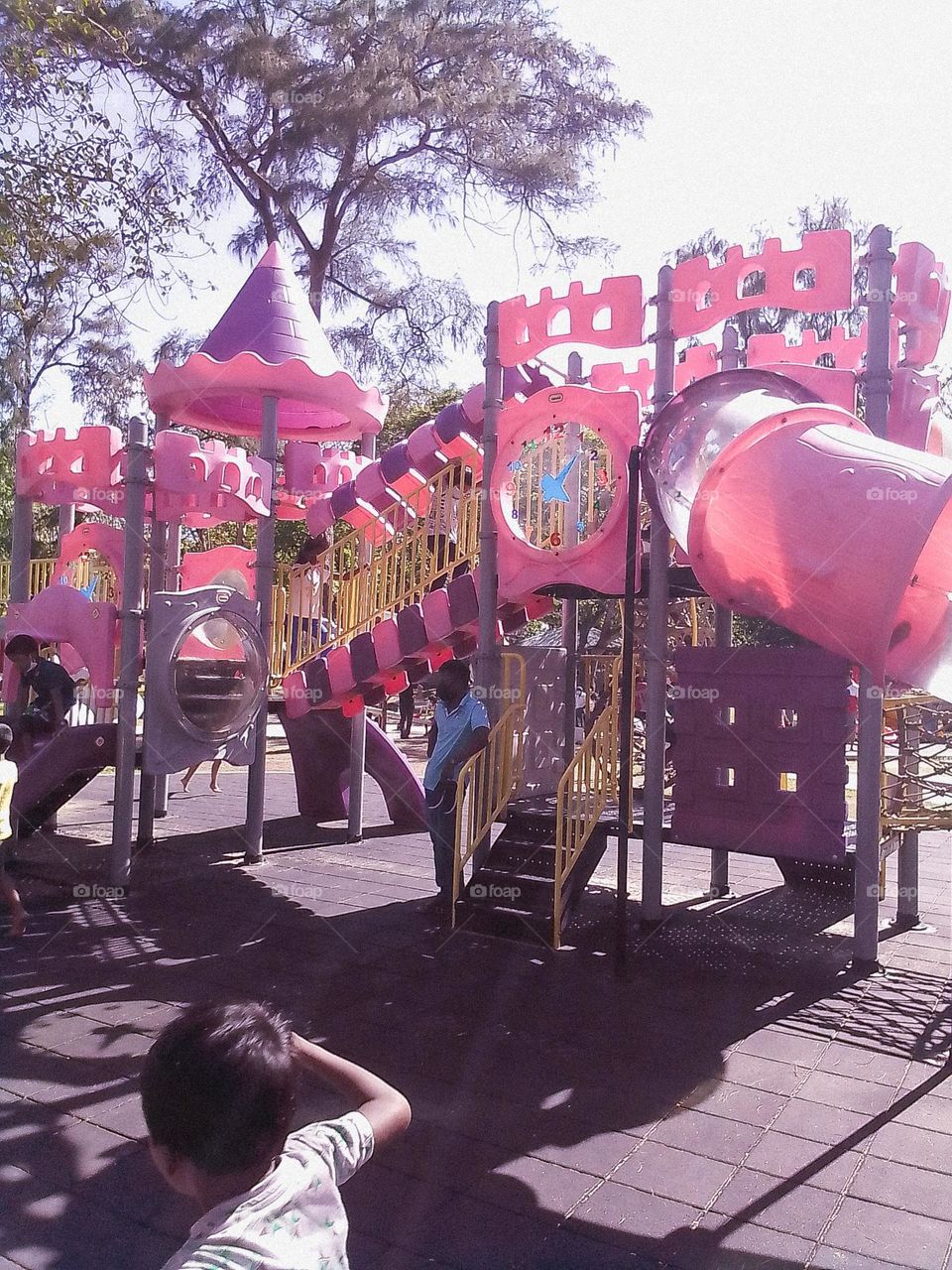 This is a capture of a children's park and there are so many items to play children. There are some children playing and one man is standing there. He is seems like a father.The playing items are in pink colour and it is to children's eye catching .