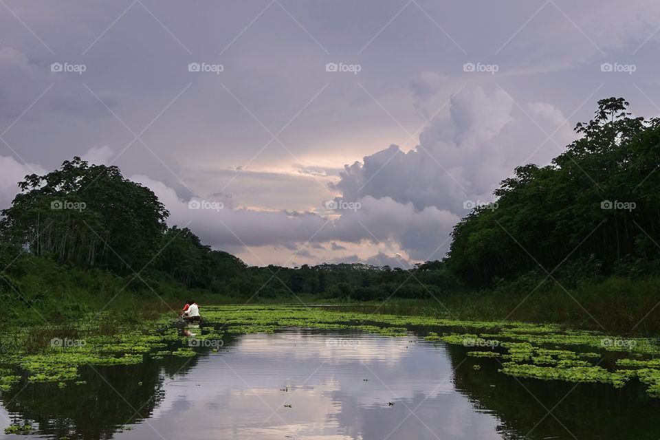 Sunset after rain, amazon river, fishing for Piranha. Cloudy skies in amazon rainforest, two fishermen near Iquitos, Peru.