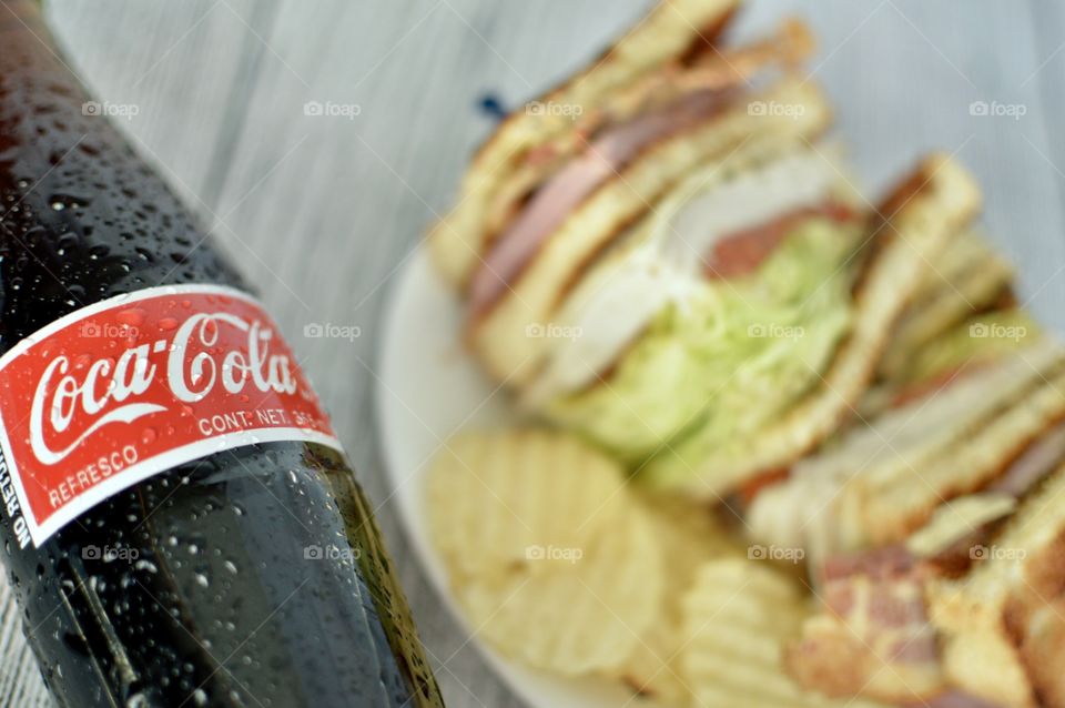 A Bottle of Coca Cola with a club sandwich on a white rustic background 