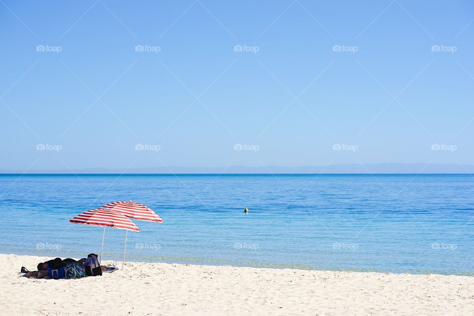 A couple is resting at the beach. Selective focus on the red and white beach umbrella.