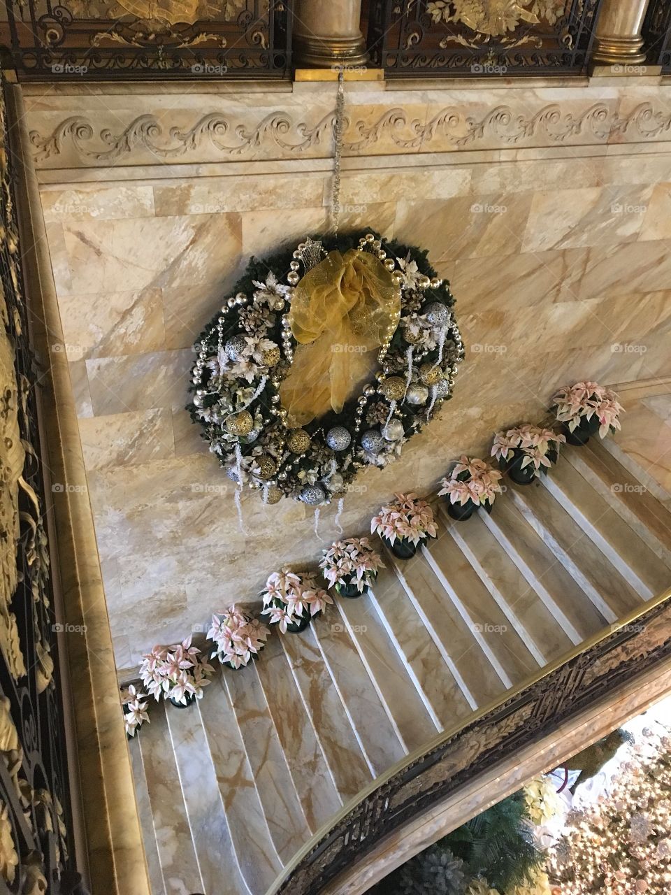 A large opulent Christmas wreath decorated a marble staircase lined with white Christmas flowers
