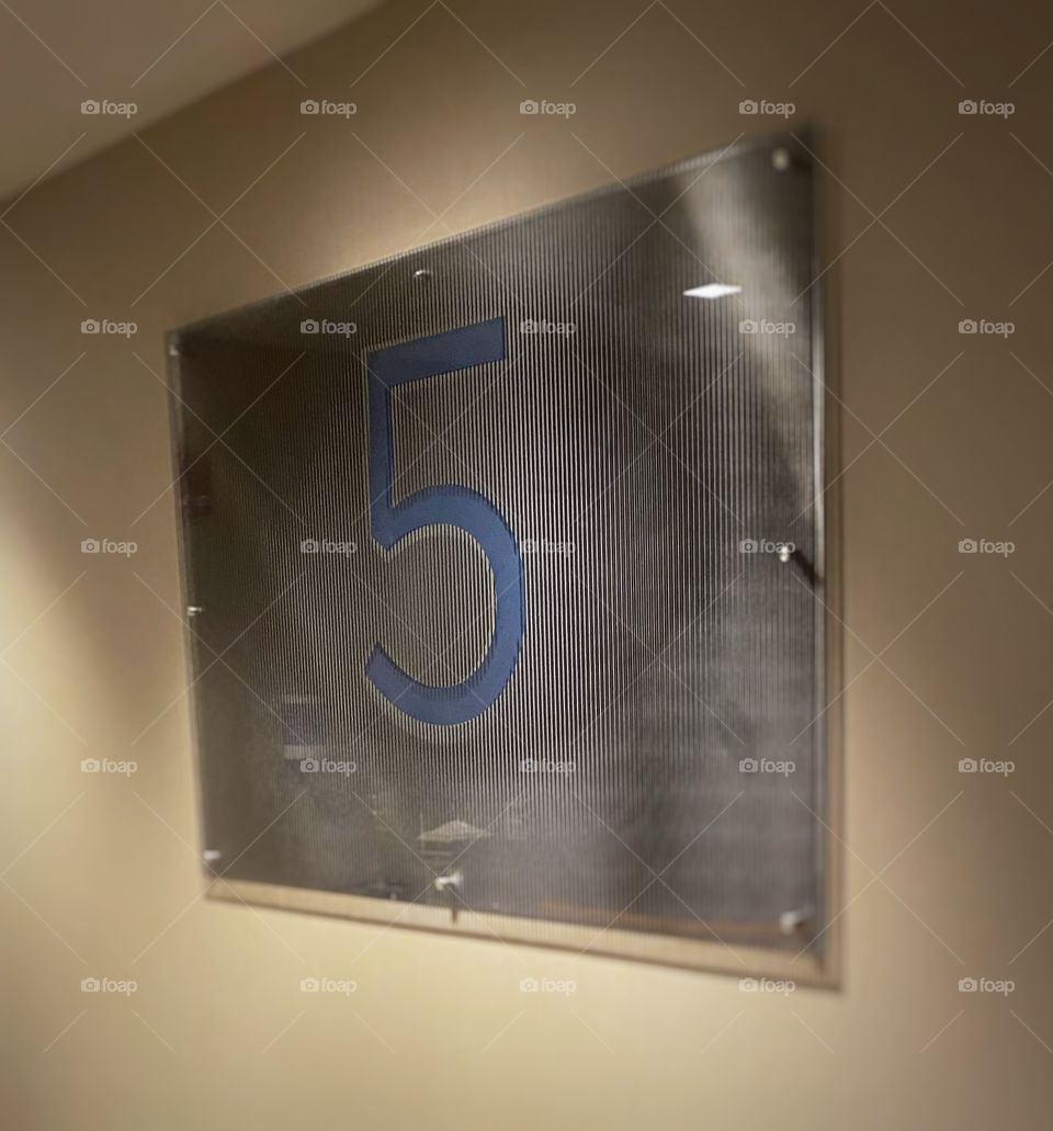 A large sign with the number 5 on it, indicating the floor level inside a hotel 