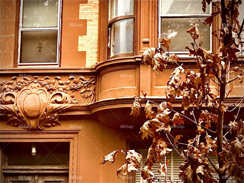 Urban detail closeup, a part of an ornamented brownstone w multilevel detail such as protruding half round room extensions. On the outside rosetta or mandala type patterns adorn the facade as well as light vs regular color bricks. 2022. Hypnotic Prod