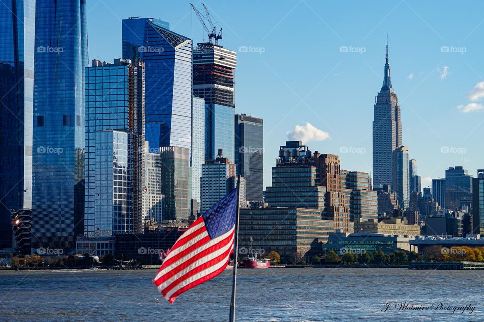 The American flag waves proudly in the foreground of Midtown Manhattan on a clear fall afternoon