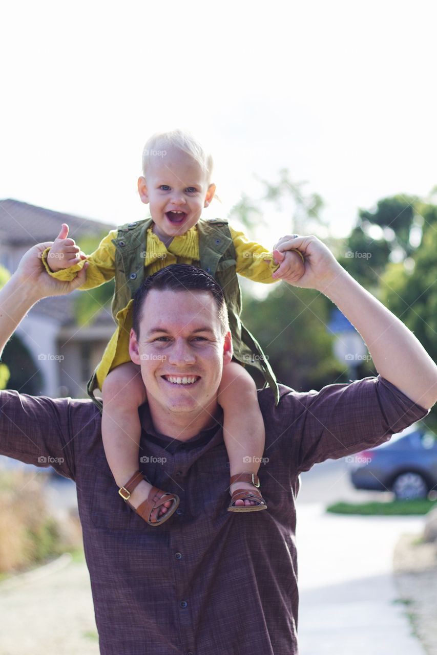 Dad gives beautiful baby girl a piggy back ride as they smile together