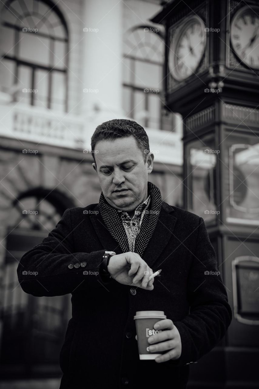 Close-up black and white portrait of a man in the city square with a clock waiting for a meeting