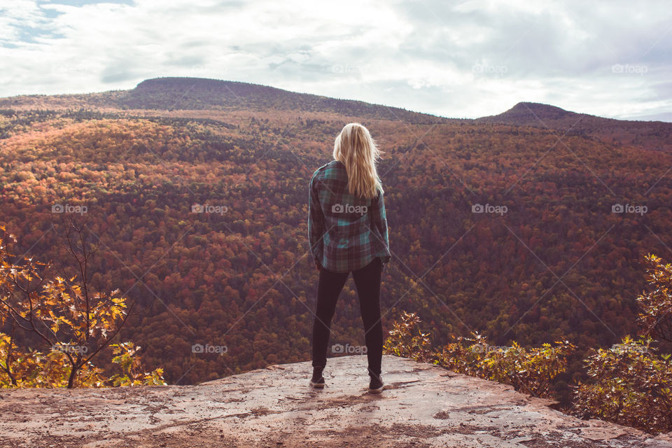 A young woman hiker looks out at the mountain range of a forest upstate New York in the Catskills mountains 
