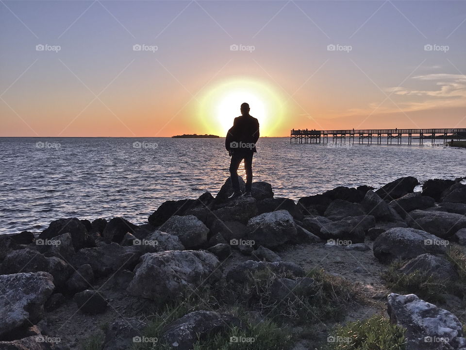 Man stands on rocks as sun sets in Gulf of Mexico 