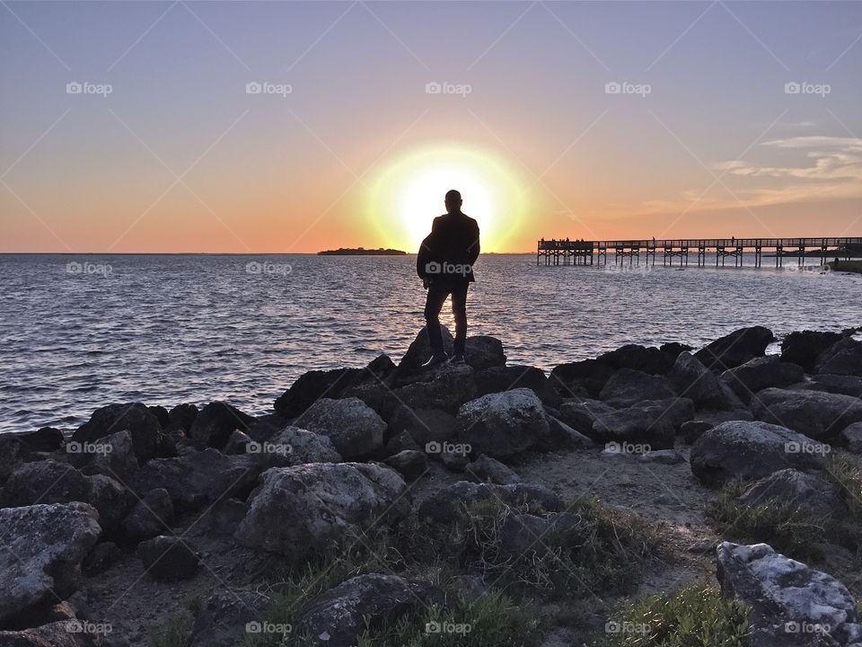 Man standing on rocks as sunsets in the Gulf of Mexico. 