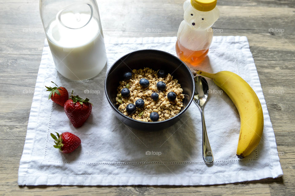 Flat lay of a smoothie bowl breakfast place setting with honey, banana, strawberry, milk  at dawn