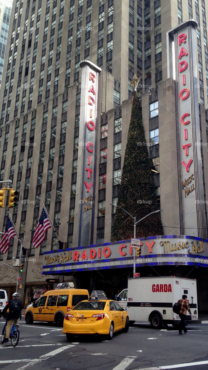 Radio City Christmas Tree with American Flags, Pedestrians, Taxis, Bicyclist, and Skyscrapers