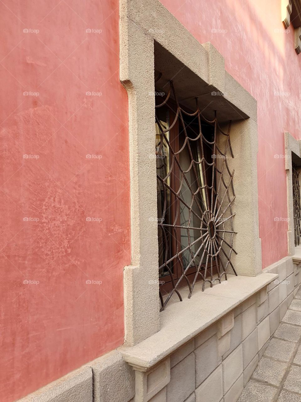 pastel pink house front with a fancy window grille - - iron spider web