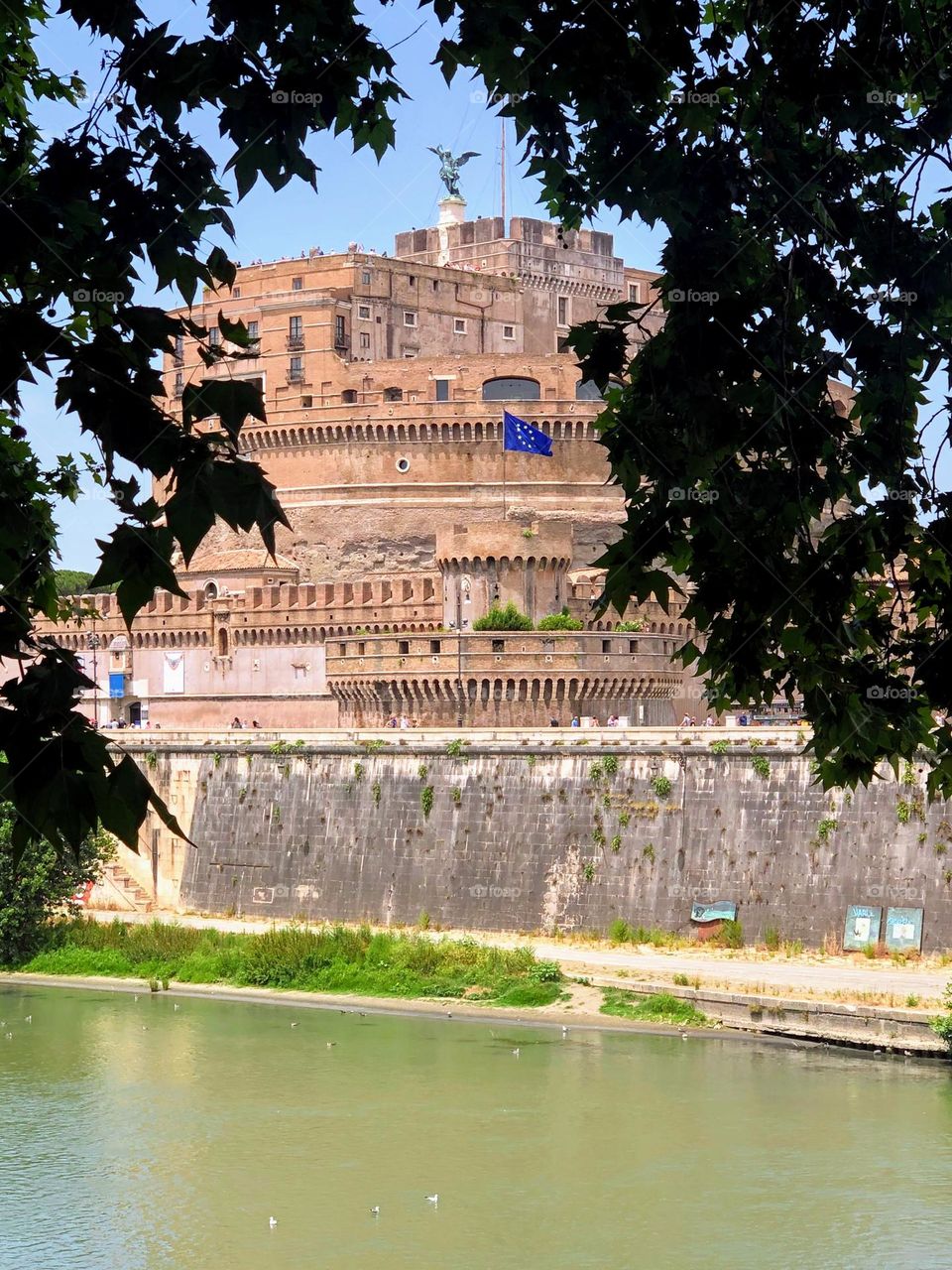 Old historical building with EU flag on the city river bank through the trees branches 