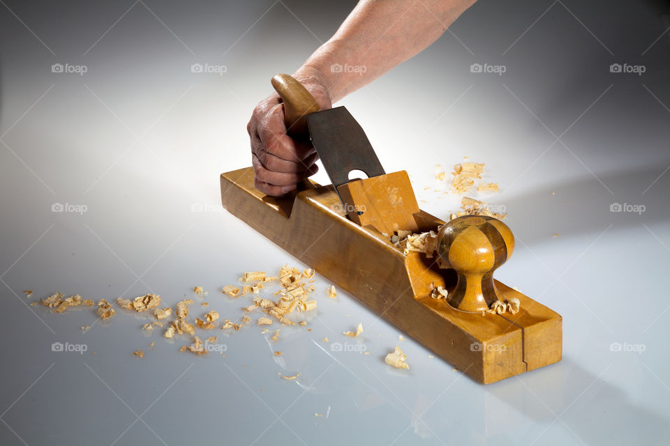 Hand of an old man holding old wooden planer with wood chips on the foreground and background.