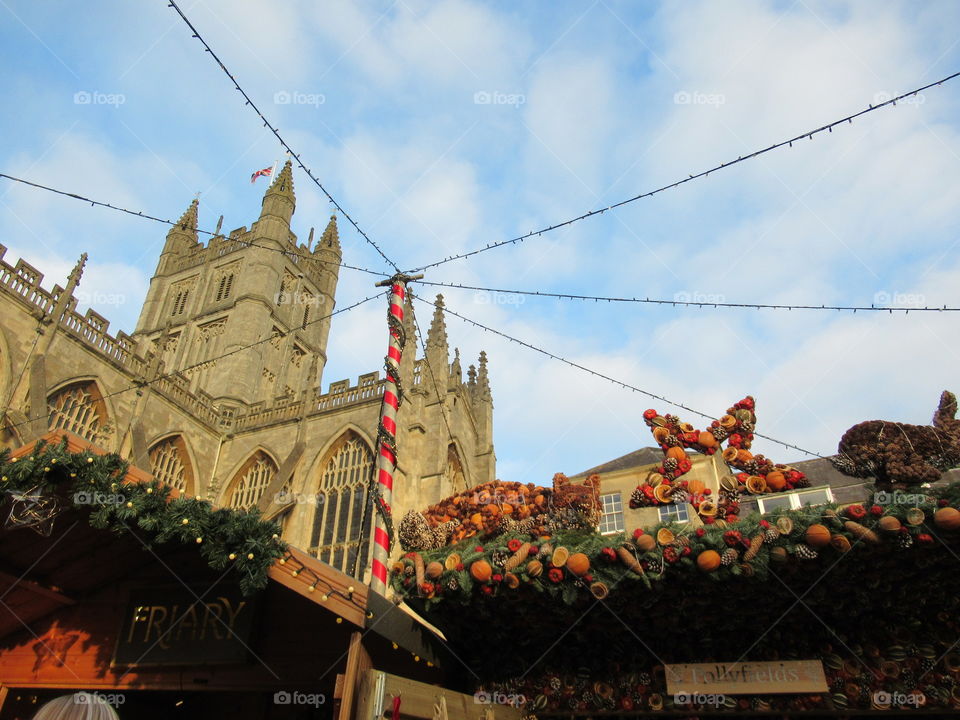 Bath Christmas market with wooden chalet roofs  with display and lights on them and Bath abbey just behind them all tops