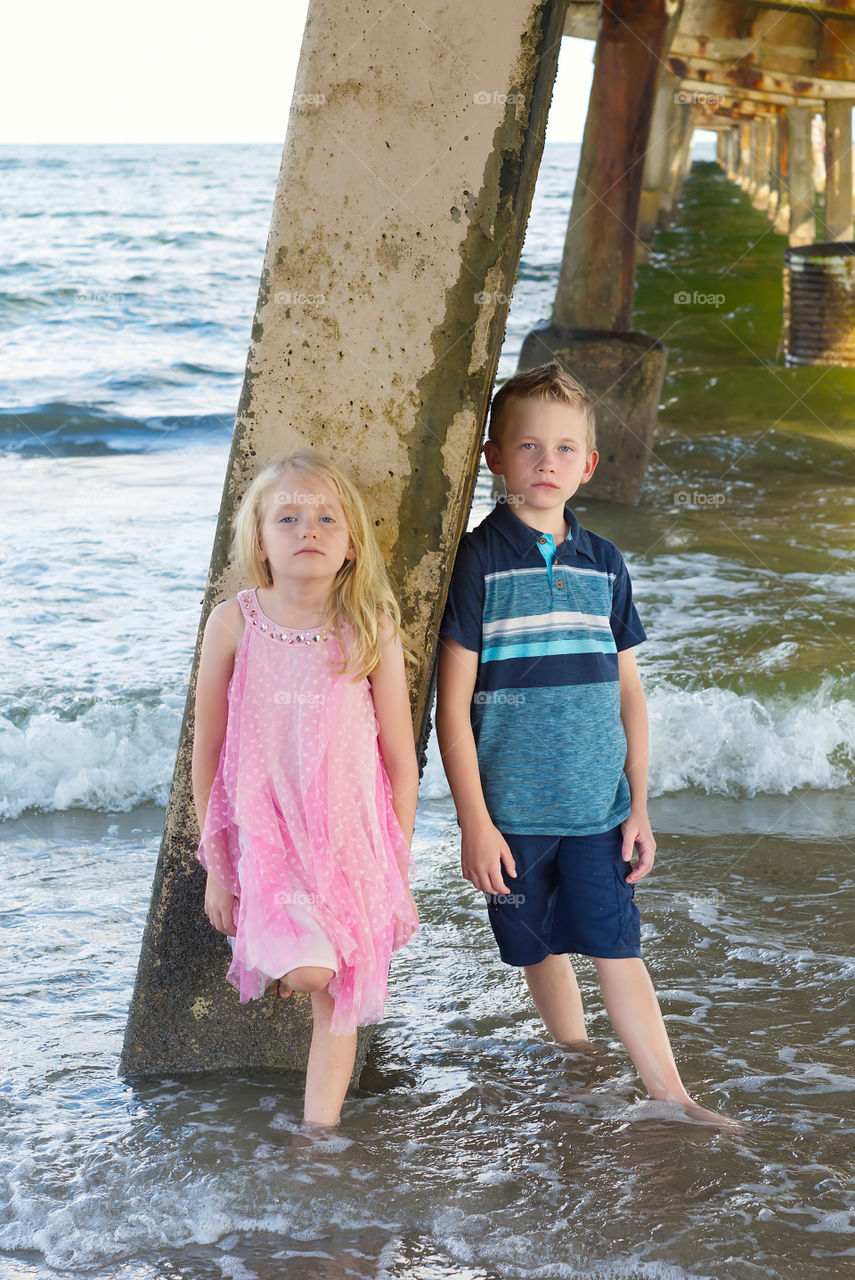 Boy girl twins model posing near a pier at the beach