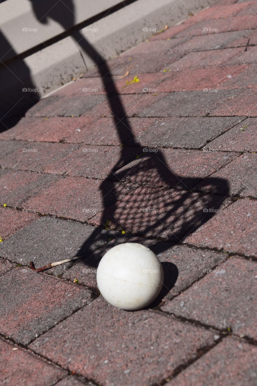 Shadow of a lacrosse stick scooping a pure white ball