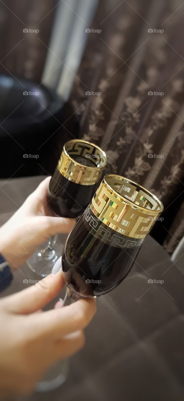 две руки с двумя позолоченными бокалами вина на фоне темных штор
