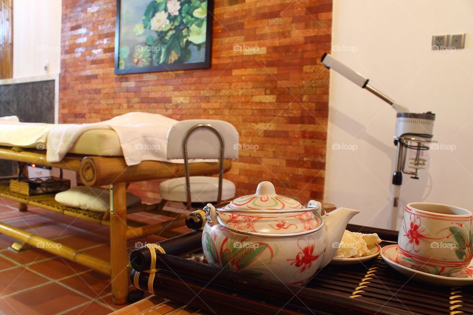 Teapot and cup of tea with candied ginger on a tray and a brown wooden table.
