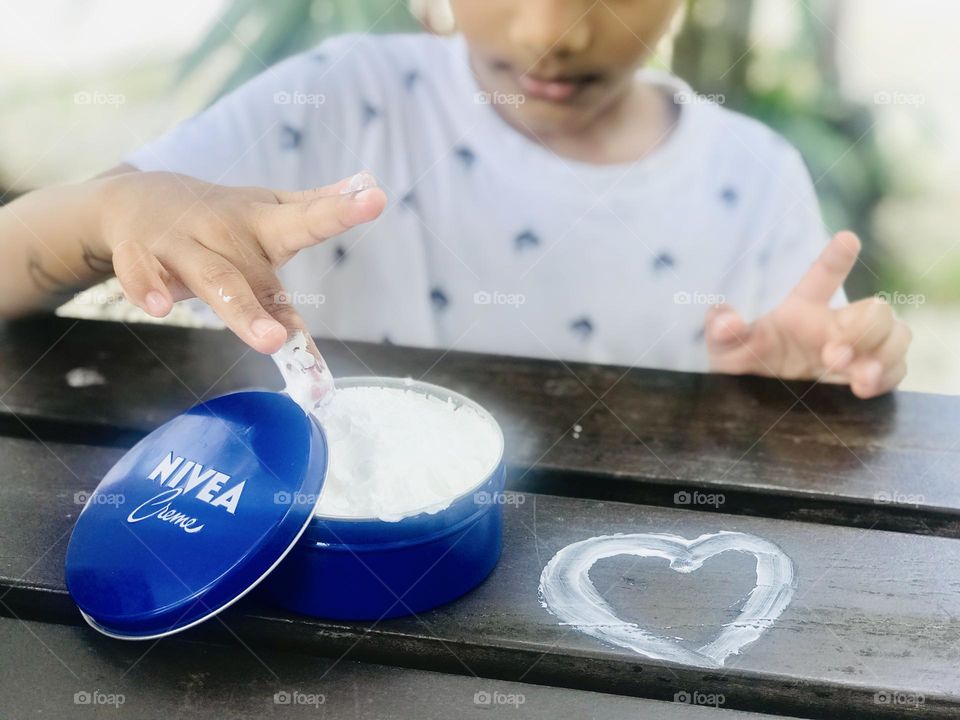 Boy with Nivea cream and draw a love symbol with white Nivea cream on a wooden table.